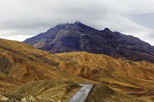 A winding road leads through a mountainous landscape under a cloudy sky