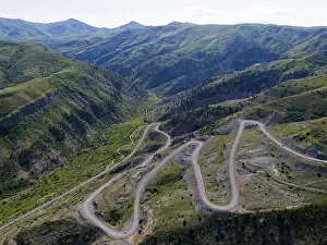 A winding serpentine road meanders through a green mountain landscape