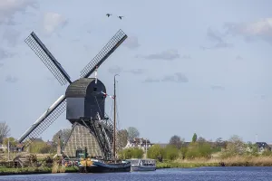 Windmill on the river bank with boats and grasses in the foreground