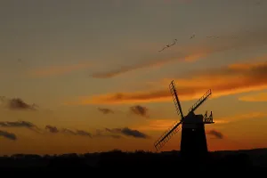 Windmill silhouette at sunset with a red sky and a skein or flock of Pink-footed geese (Anser brachyrhynchus)