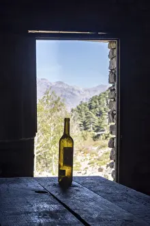An empty wine bottle on a wooden table in front of an open door with a view of the mountains