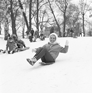 Winter in the 1960s. A young woman is sliding down a hill on a saucer shaped type plastic pulk