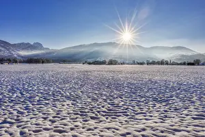Winter landscape with snow-covered field and rising sun against a mountain backdrop