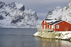 Wintery, Nordic landscape with red holiday home standing directly by the fjord
