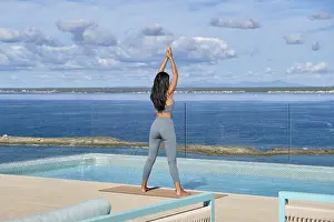 Framed Print : A woman in active wear performs yoga by an infinity pool overlooking the ocean on a terrace