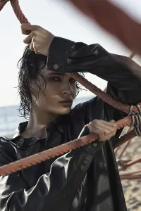 A woman in a black leather jacket holds onto ropes on a sunny beach