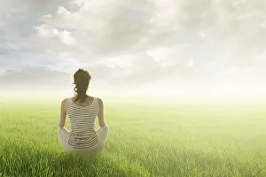 Woman of brunet hair sit on grassland against sunrise or sunset