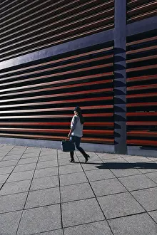 Framed Print : A woman in casual attire walks by a modern building with distinctive horizontal slats Framed Print : A woman in casual attire walks by a modern building with distinctive horizontal slats