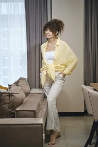 A woman is casually dressed in a yellow shirt and beige pants while standing next to a sofa in a stylish interior