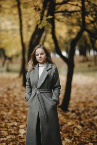 A woman in a coat stands in an autumn forest with fallen leaves