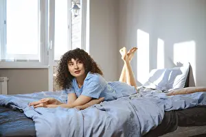 A woman with curly hair lays on a bed with light blue sheets