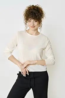 Woman with curly hair stands smiling with gracefully placed hands