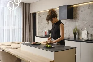 A woman cuts the skin crosswise on a duck breast standing in a kitchen