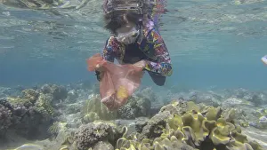 Woman in diving equipment swims and collects plastic debris underwater on the bottom of coral reef