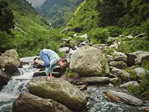Woman doing Kakasana asana, crow pose arm balance outdoors at tropical waterfall