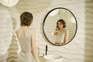 A woman dressed in a shimmering top stands in front of a round mirror
