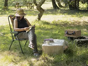 Woman enjoying a peaceful afternoon reading a book in a folding chair under a tree