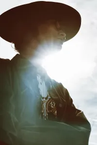 A woman in a hat and sunglasses stands against the sky