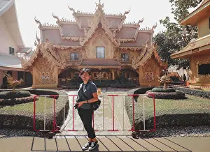A woman posing in front of an ornate traditional thai temple with landscaped garden in Wat Rong Khun or White Temple