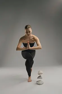 A woman practices yoga, balancing on one leg while holding a prayer position with her hands
