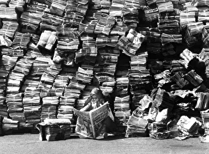 Woman reads newspaper in front of a big pile of newspapers