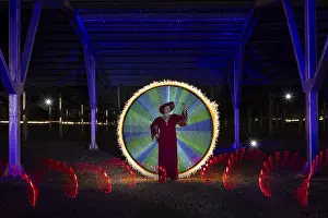 A woman with a red dress and hat stands in the middle of an impressive light painting under a canopy
