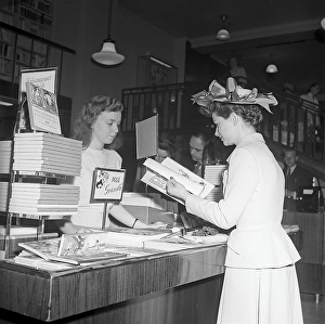Woman shopping for books in 1948. A young woman in a neatly matching jacket and skirt with a creatively designed hat, in a shop. She has stopped in the book section and is looking through Goesta Knutsson's latest book about Pelle Svansloes