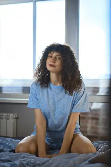 A woman sits on a bed in front of a large window
