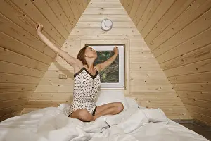 A woman sits on a bed in a wooden cabin