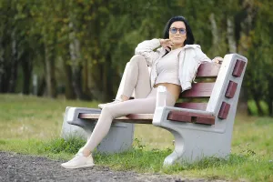 A woman sits on a park bench dressed in light-colored casual clothes
