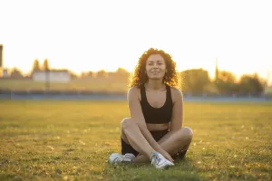 A woman is sitting cross-legged on grass in sportswear during sunset