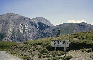 Woman sitting at sign for Col d'Allos 2250m Alpine pass, Alpes-de-Haute-Provence, France 1974
