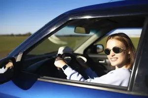 Woman smiling in a blue car while driving on a rural road