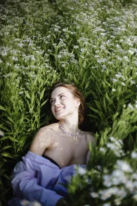 A woman smiling in a field of tall green plants with delicate white flowers under bright sunlight