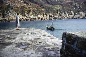 Woman standing on the quay looking at a fishing boat, Lamorna Cove, Cornwall, England, UK November 1961