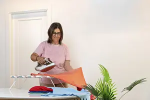 Woman standing smiling while ironing a colorful t shirt on an ironing board
