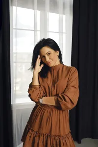 A woman stands elegantly by a large window