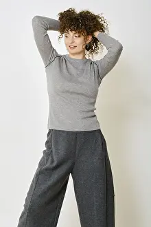 A woman stands with her hands behind her head