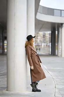 A woman stands leaning against a concrete column in an urban setting