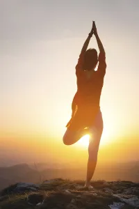 A woman stands in a yoga pose against the sun in the mountains
