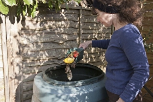 Woman throws vegetable waste into the compost bin in the garden