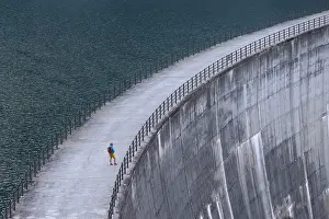 Woman, walking alone along a large dam with a view of the endless expanse of water