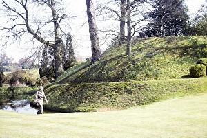 Woman walking past the hill of the Norman castle Motte and Bailey, Abinger, Surrey, England, UK 1980