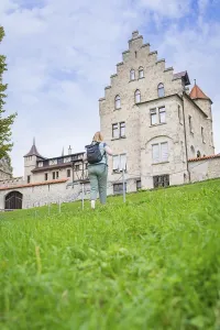 Framed Print : A woman walks up a grassy hill towards an imposing historic castle