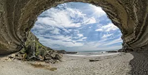 Woman wandering through the mighty rock overhang of Truman's Cove on the beach with a waterfall
