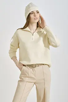 A woman wearing a light cream sweater and beige trousers