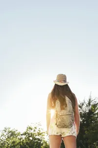 A woman wearing a sun hat and backpack enjoys a sunny day hike