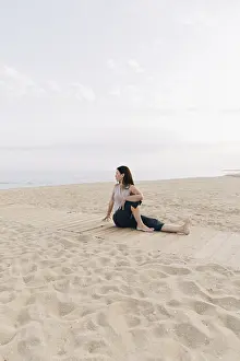 A woman in a yoga pose on a sandy beach is executing the Ardha Matsyendrasana