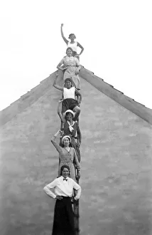 Six women standing on a ladder in front of a house waving