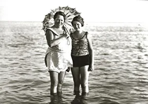 Two women in swimsuits and with parasol standing in the sea